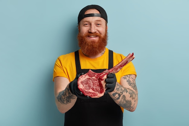 Bezpłatne zdjęcie rzeźnik człowiek z imbirową brodą trzymając mięso