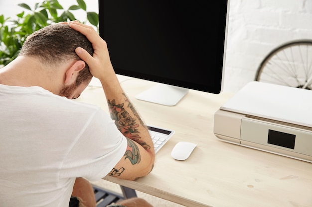 Sad freelancer ma ciężki projekt i trzyma głowę w dłoniach, siedząc przed działającym ekranem komputera Widok z boku