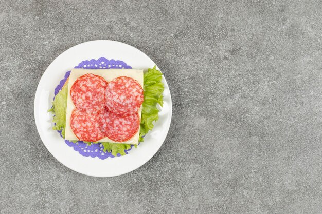 Bezpłatne zdjęcie salami pokrojone w plasterki na białym talerzu z serem i sałatą