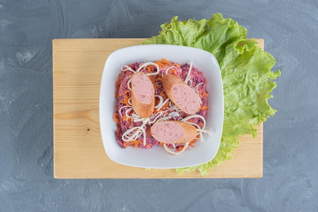 Bezpłatne zdjęcie salaterka z orzechów i buraków na drewnianej desce z liściem sałaty, zwieńczona kiełbasą i serem na marmurowym stole.