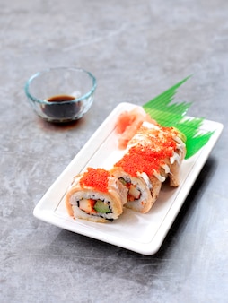 Salmon blaze sushi roll, paluszek krabowy, ogórek i łosoś pieczony posypane tobiko. podawane na białym prostokątnym talerzu.
