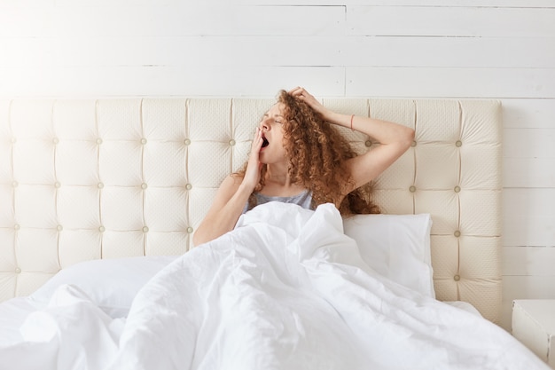 Bezpłatne zdjęcie salowy strzał pokojowa atrakcyjna młoda dama relaksuje w jej łóżku w ranku