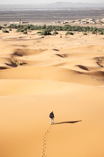 Samotna osoba spacerująca po pustyni w pobliżu wydm w słoneczny dzień