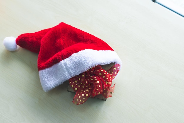 Santa claus kapelusz z pudełka na prezenty umieszczone na drewnianym stole wnętrze pokoju widok przez okno z drzewa tło z miejsca kopiowania, dekoracja podczas świąt bożego narodzenia i nowego roku.