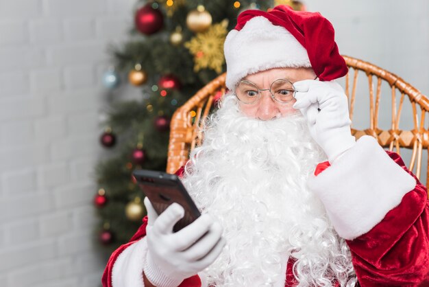 Santa siedzi na bujanym fotelu i patrząc na telefon