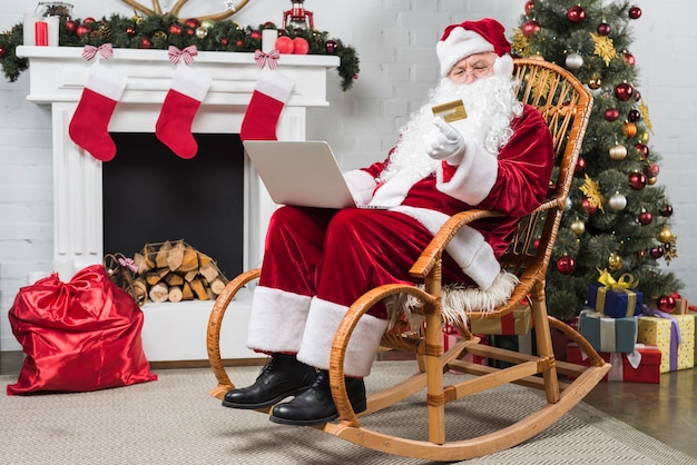 Santa siedzi na bujanym fotelu z laptopa