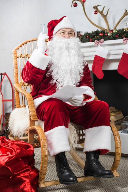 Santa siedzi w bujanym fotelu z listy życzeń i długopis