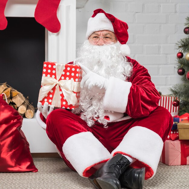 Santa w okularach siedzi z pudełka na podłodze