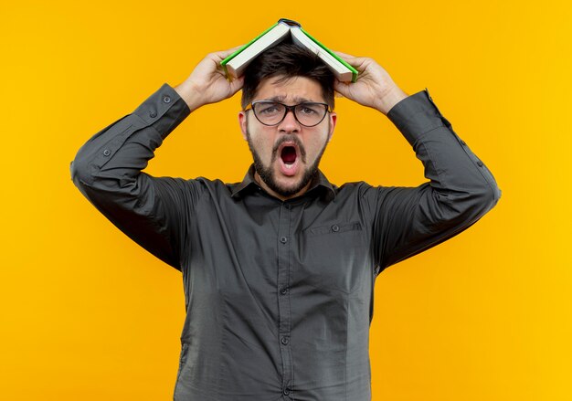 Scared młody biznesmen w okularach zakrytej głowy z książką na żółtym tle