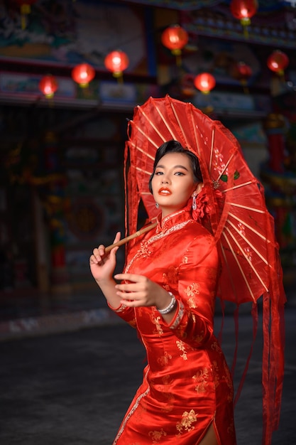 Scena nocna, Portret Azjatycka piękna kobieta ubrana w cheongsam uśmiechnięta i pozuje z papierowym czerwonym parasolem w świątyni w Chiński Nowy Rok