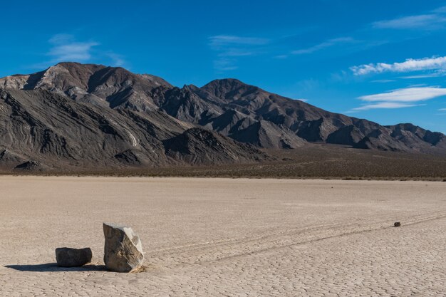 Scena pustynna z długim śladem pozostawionym przez dwa kamienie na suchej ziemi i wzgórza z tyłu