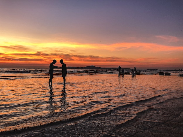 Sceneria zachodu słońca z sylwetkami ludzi na plaży
