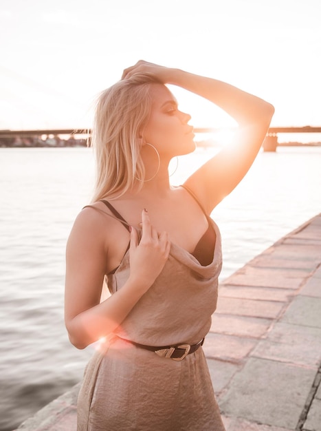Seksowna młoda kobieta w Body pozuje dla fotografa na zachód słońca nad rzeką.