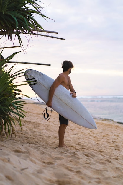 Bezpłatne zdjęcie seksowny surfer surfing człowiek z deską surfingową. przystojny młody sportowiec mężczyzna trzyma deskę surfingową z mokrymi włosami na wakacje sport lato plaża. sportowy cel podróży. styl życia surfingu.