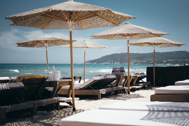 Selektywne szerokie ujęcie brązowych drewnianych leżaków pod parasolami przy plaży