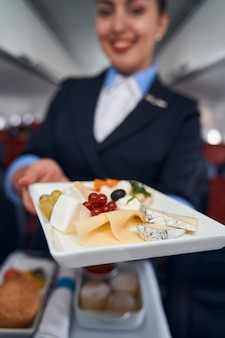 Ser i owoce na jednorazowym talerzu w ręku stewardessy, trzymającej go przed kamerą