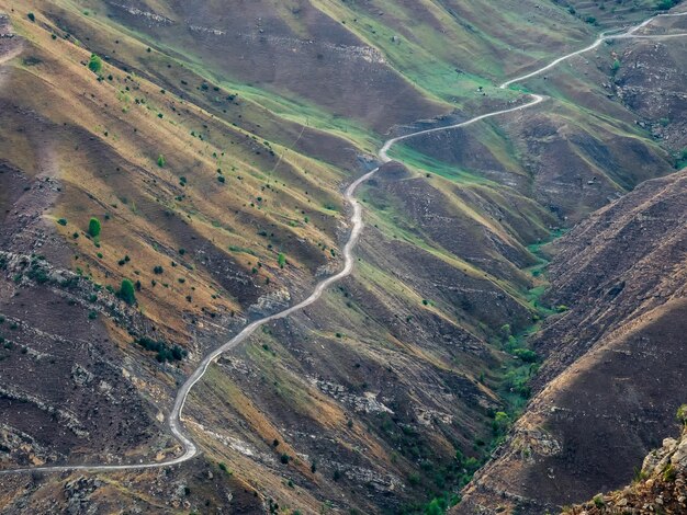 Serpentyna górska przez prążkowane szczyty górskie. niebezpieczna, wąska, górska droga gruntowa przez wzgórza prowadzi do wysokogórskiej wioski w dagestanie. widok z lotu ptaka.
