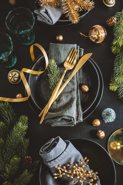Serwowane nakrycie bożonarodzeniowe w ciemnych odcieniach ze złotą dekoracją.