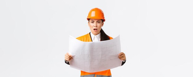 Sfrustrowana i niezadowolona kobieta azjatycki inżynier główny architekt w strefie budowy, wyglądająca na rozczarowaną po przestudiowaniu planów, gapi się na aparat besztający kierownika białe tło