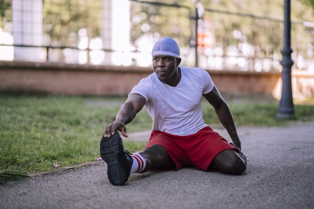 Shallow focus shot of African-American samiec w białej koszuli, rozciągający się w parku