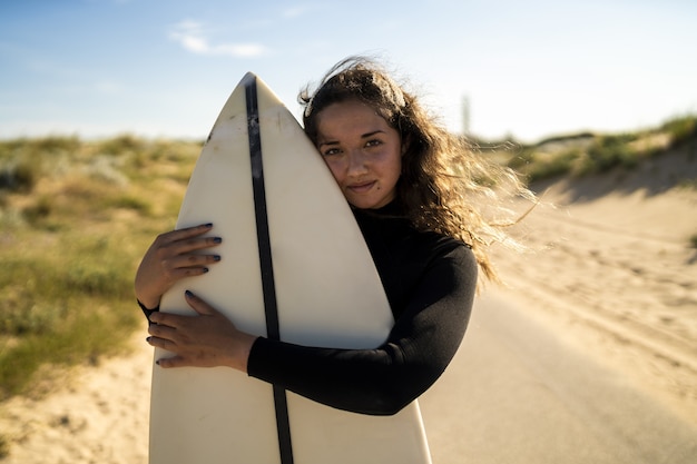 Shallow focus strzał z atrakcyjną kobietą przytulanie deskę surfingową na środku drogi