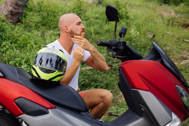 Siłacz na polu tropikalnej dżungli z czerwonym motocyklem