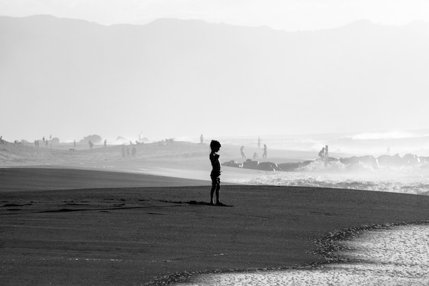 Skala szarości strzał młodego chłopca na piaszczystym brzegu morza w pobliżu morza
