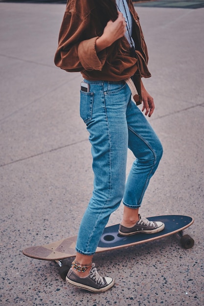 Bezpłatne zdjęcie skater dziewczyna w dżinsach jeździ na swoim longboardzie w parku.