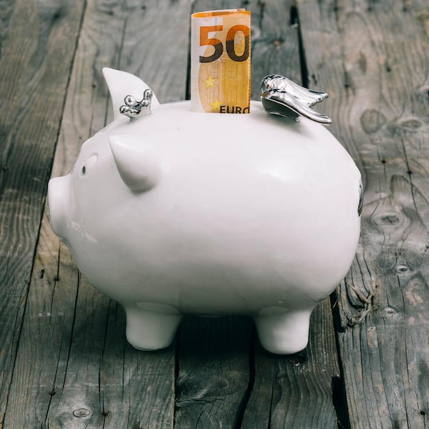 Składał pięćdziesiąt euro notatkę w szczelinie biały piggybank na drewnianym stole