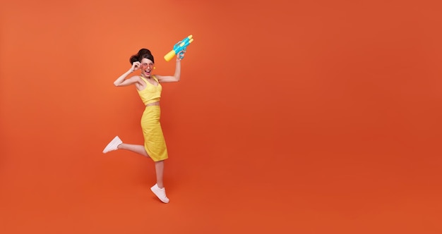 Skoki Młoda kobieta szczęśliwa piękność z pistoletem na wodę i podczas festiwalu Songkran studio strzał na pomarańczowym tle kopii