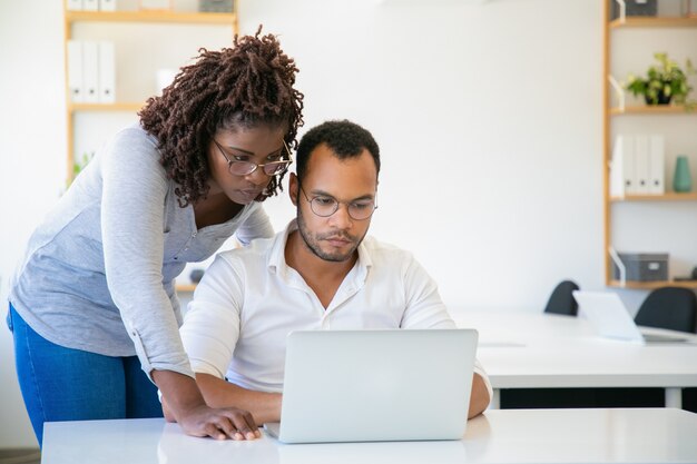 Skoncentrowana amerykanin afrykańskiego pochodzenia kobieta patrzeje laptop