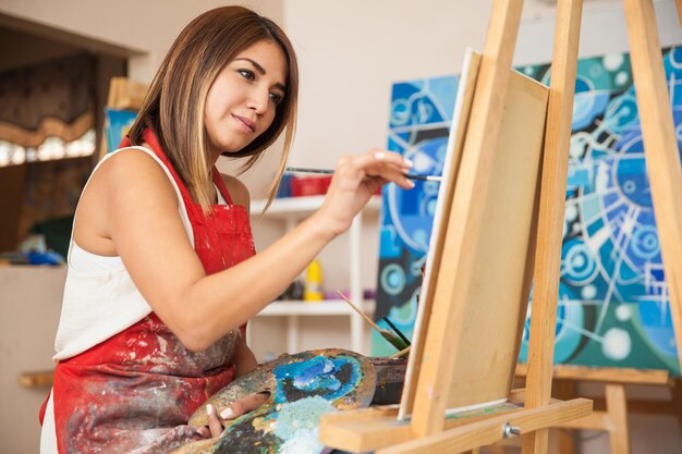 Skoncentrowana młoda artystka pracująca nad nowym obrazem w swoim warsztacie