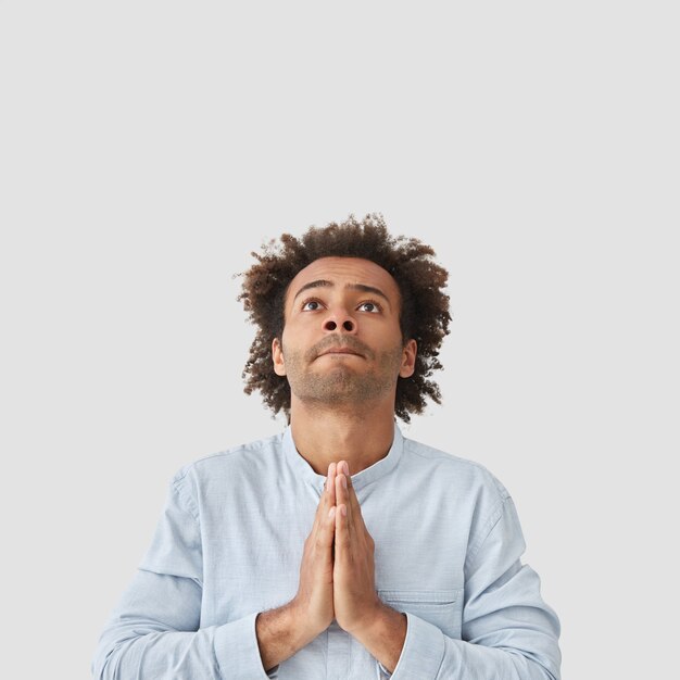 Skoncentrowany atrakcyjny mężczyzna student wykonuje gest modlitwy, patrzy z nadzieją w górę