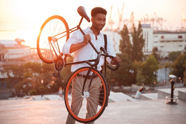 Skoncentrowany młody afrykański mężczyzna w wczesnym poranku z bicyklem