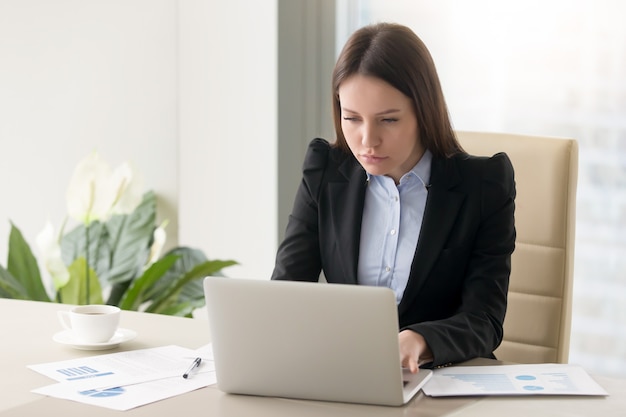 Skoncentrowany poważny bizneswoman robi raportowi, pracuje z laptopem w biurze