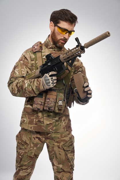 Skoncentrowany żołnierz armii w mundurze przeładowującym broń karabinową w studiu