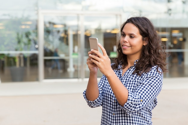 Skupiająca się uśmiechnięta studencka dziewczyna z smartphone konsultuje internet