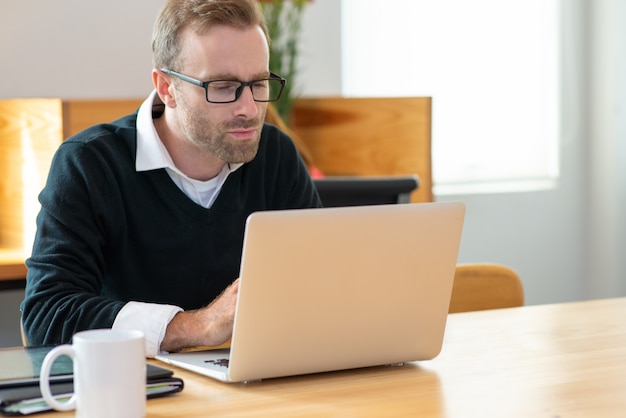 Skupiający się w średnim wieku biznesowy mężczyzna pracuje na laptopie.