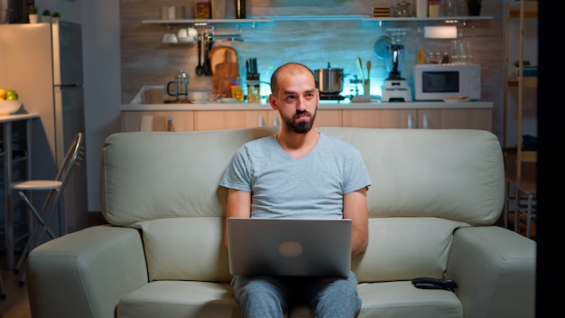 Skupiony mężczyzna siedzący na kanapie i piszący projekt online na laptopie