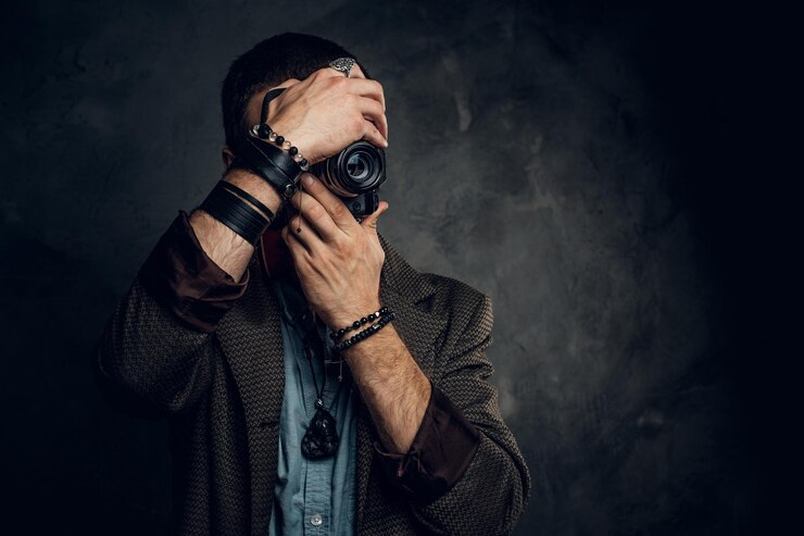 Bezpłatny plik Zdjęcie skupiony młody fotograf robi zdjęcie na ciemnym tle grunge.
