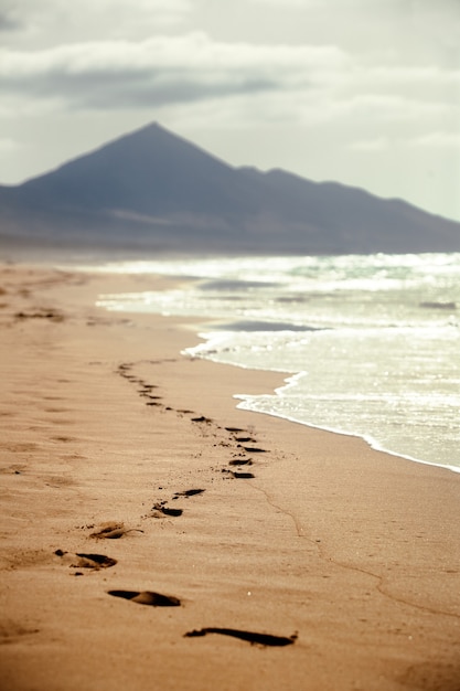 Ślady stóp na piaszczystej plaży z górą w tle na Wyspach Kanaryjskich, Hiszpania