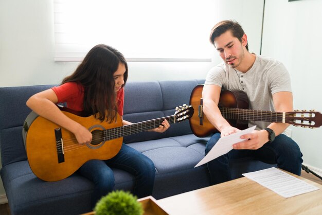 Śledź nuty. Nauczyciel muzyki latynoskiej rozmawiający z uczniem o graniu piosenki na gitarze akustycznej podczas lekcji domowych