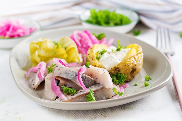 Śledź z pieczonym ziemniakiem, cebulą i ogórkiem kiszonym na talerzu. kuchnia tradycyjna.