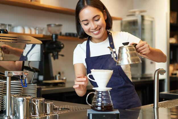 Śliczna brunetka dziewczyna barista personel kawiarni nalewa wodę z czajnika i warzenia kawy z filtrem za cou