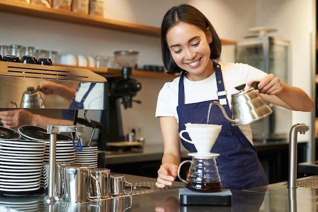 Bezpłatne zdjęcie Śliczna brunetka dziewczyna barista personel kawiarni nalewa wodę z czajnika i warzenia kawy z filtrem za cou