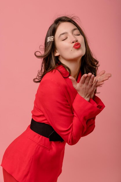 Śliczna kaukaska dama w wieku 20 lat w czerwonej kurtce wysyła pocałunek do aparatu na różowym tle Koncepcja stylu życia