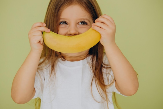 Bezpłatne zdjęcie Śliczna mała dziewczynka na białym tle z bananem