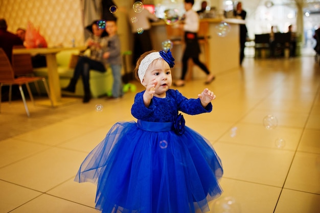 Bezpłatne zdjęcie Śliczna mała dziewczynka w niebieskiej sukience bawi się bańkami mydlanymi 1 rok urodzin!