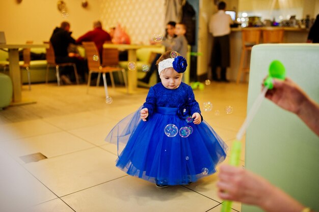 Śliczna mała dziewczynka w niebieskiej sukience bawi się bańkami mydlanymi 1 rok urodzin!