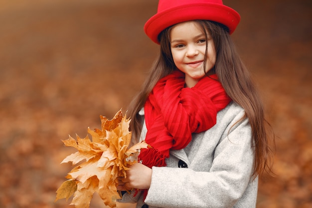 Śliczna mała dziewczynka w szarym żakiecie bawić się w jesień parku
